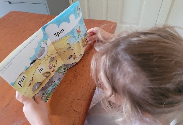 An image with a girl, approximate age 5, reading a colourful decodable book.